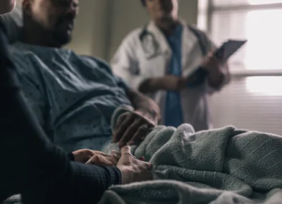 man-in-hospital-bed-comforted-by-friend-as-doctor-looks-on